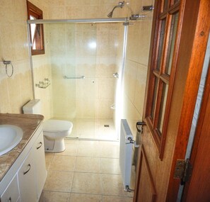 A bathroom with a shower, toilet, sink, and a wooden door. - Bella Casa Condominio Centro Gramado (Gramado)