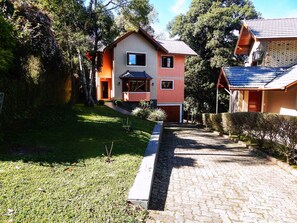 A two-story house with a brick facade, a small front porch, and a paved driveway leading to a garage. - Bella Casa Condominio Centro Gramado (Gramado)