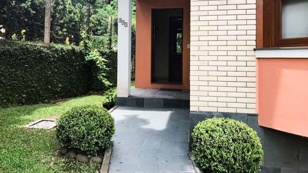 Une entrée d’immeuble avec un chemin pavé, un petit espace jardin et une haie.