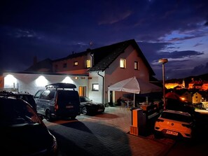 A parking area with multiple cars, a building with a sloped roof, and a white umbrella providing shade. - Penzion Hornička (Cesky Krumlov)