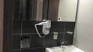 Un baño moderno con lavamanos blanco, paredes con azulejos oscuros, un espejo y una zona de ducha.