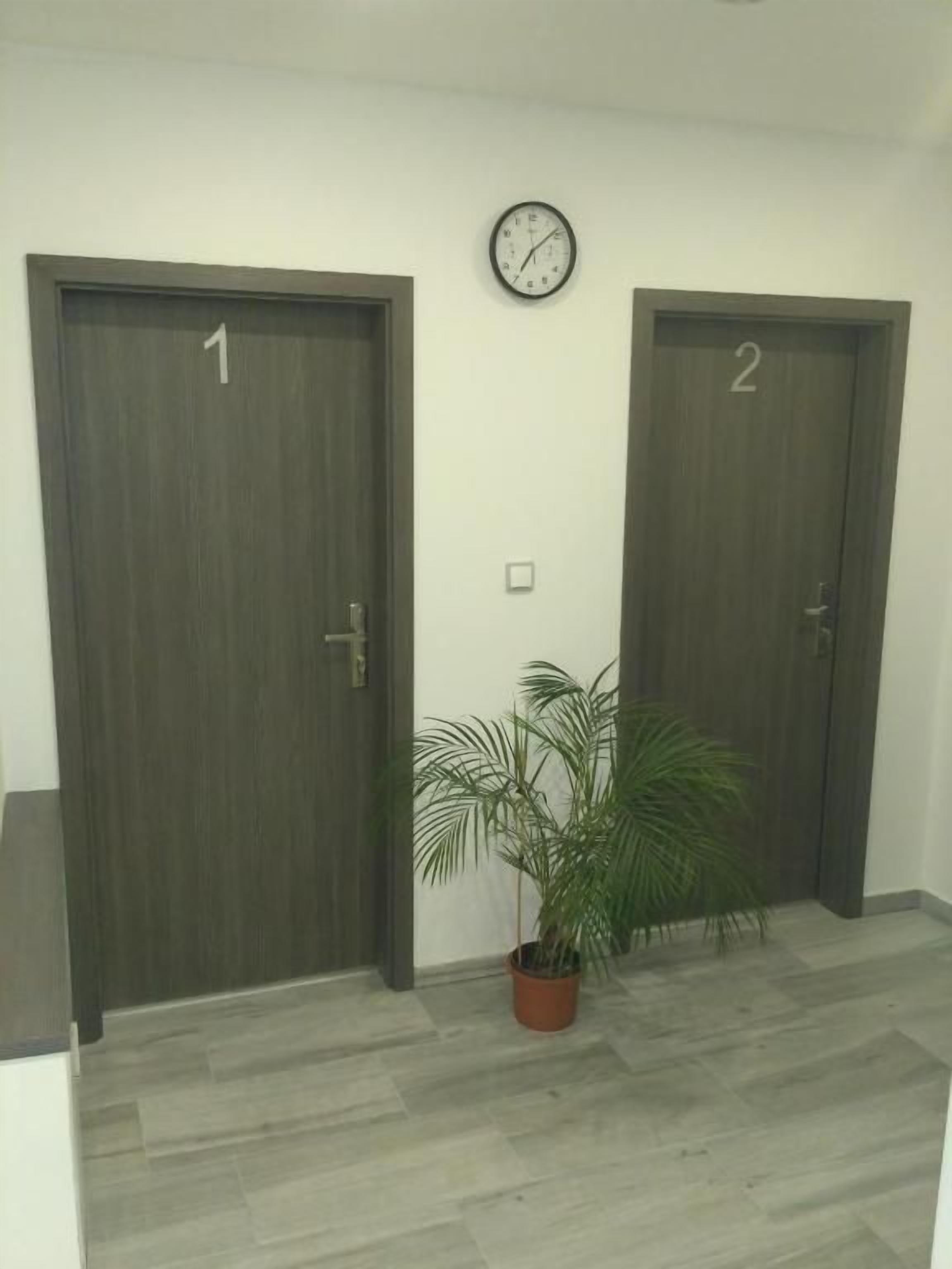 Dos puertas con los números 1 y 2, una planta en maceta y un reloj de pared.