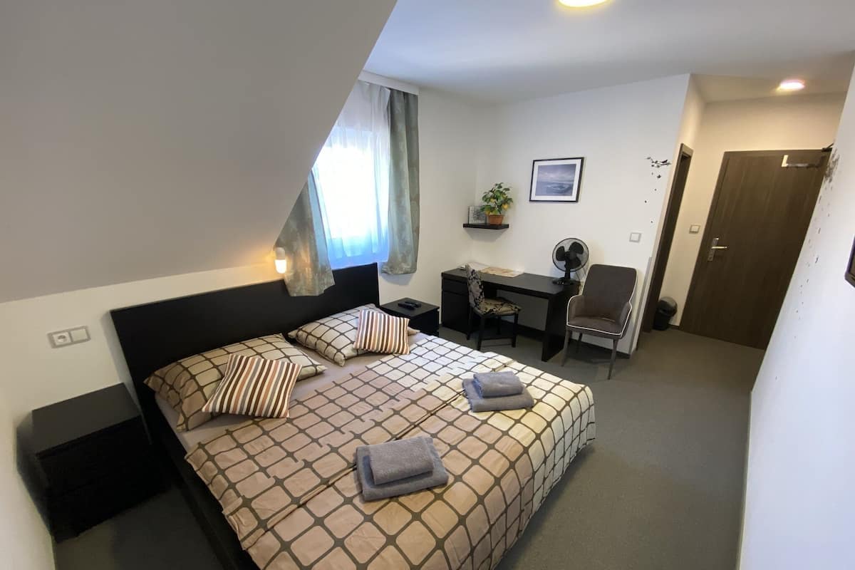 A bedroom with a bed, a desk, a chair, a fan, and a door.
