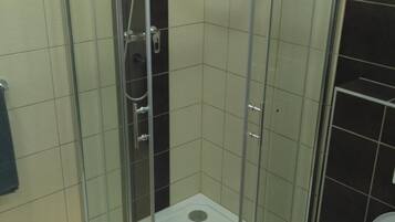 A glass-enclosed shower stall with a white floor, a visible showerhead, and a toilet to the right.