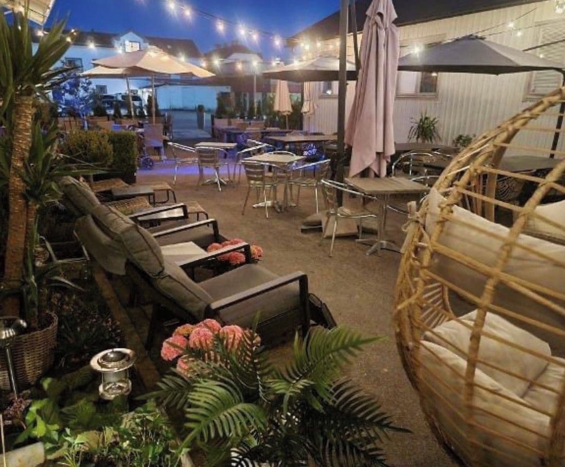 An outdoor seating area with tables and chairs, surrounded by plants and umbrellas.