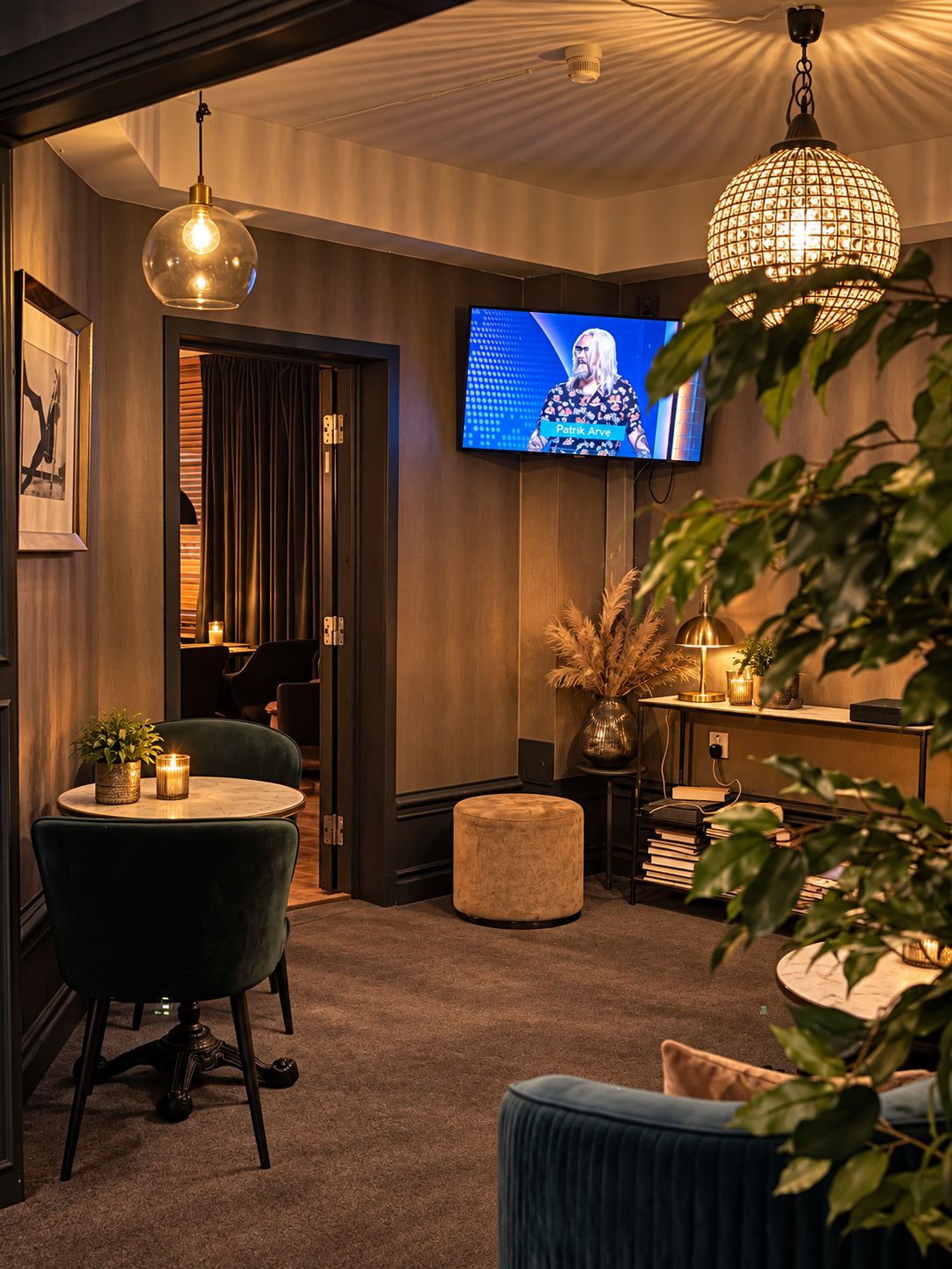 A cozy room with a television, a round table with a chair, a small ottoman, and a decorative lamp.