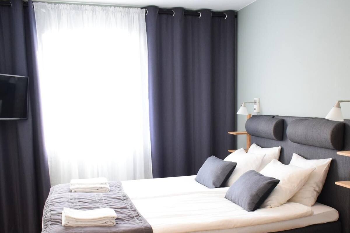 Ein modernes Hotelzimmer mit einem großen Bett, einem Nachttisch mit Lampe und einem an der Wand befestigten Fernseher.