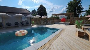 Eine Holzterrasse mit Pool, Sitzgelegenheiten im Freien und Sonnenschirmen.