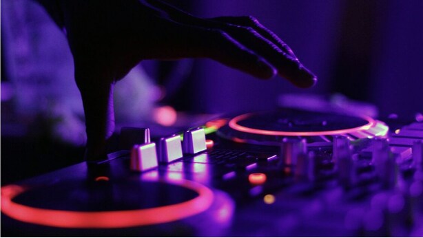 Close-up van een DJ die muziek mixt, met een draaitafel en mengpaneel, verlicht met paars licht.