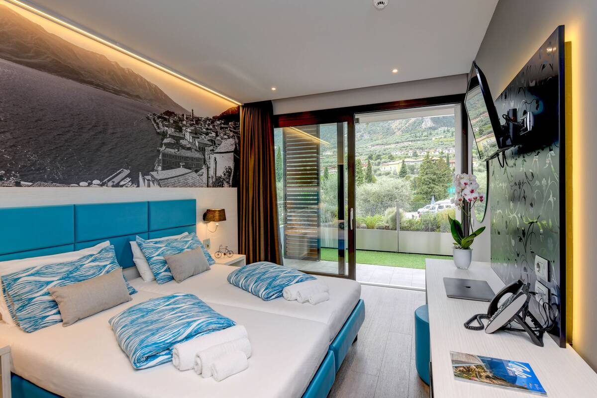 Habitación de hotel moderna con una cama grande, un escritorio con una computadora portátil y vistas a un paisaje montañoso a través de una puerta corredera de vidrio.