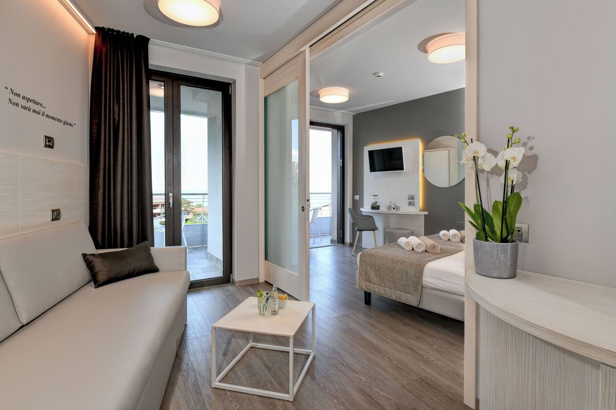 Una habitación de hotel moderna con sofá, una mesita, cama, escritorio y balcón con vistas.