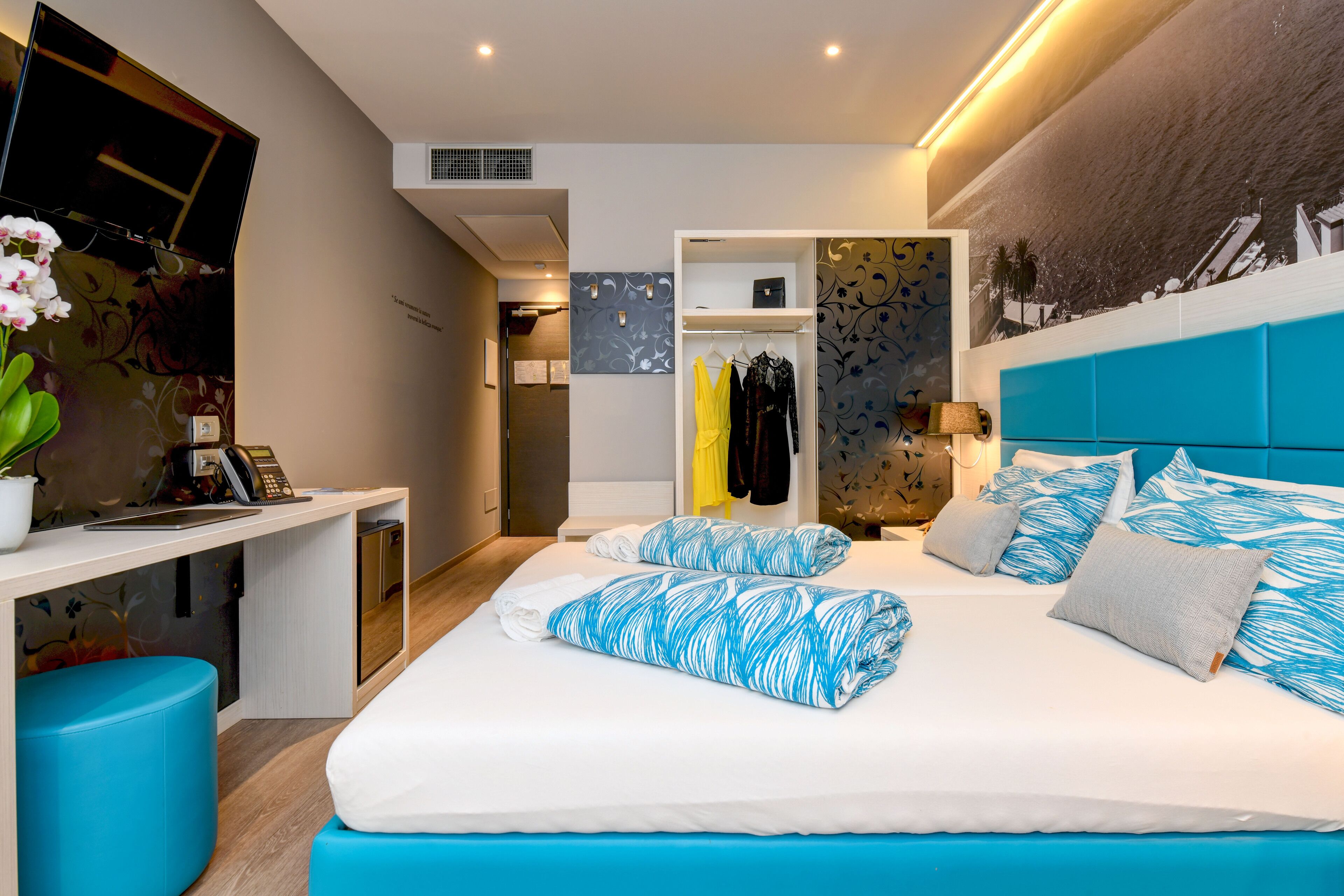 Una habitación de hotel moderna con una cama grande, un escritorio con ordenador, un armario y un televisor fijado a la pared.