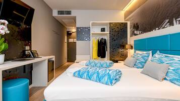 Una habitación de hotel moderna con una cama grande, un escritorio con ordenador, un armario y un televisor fijado a la pared.