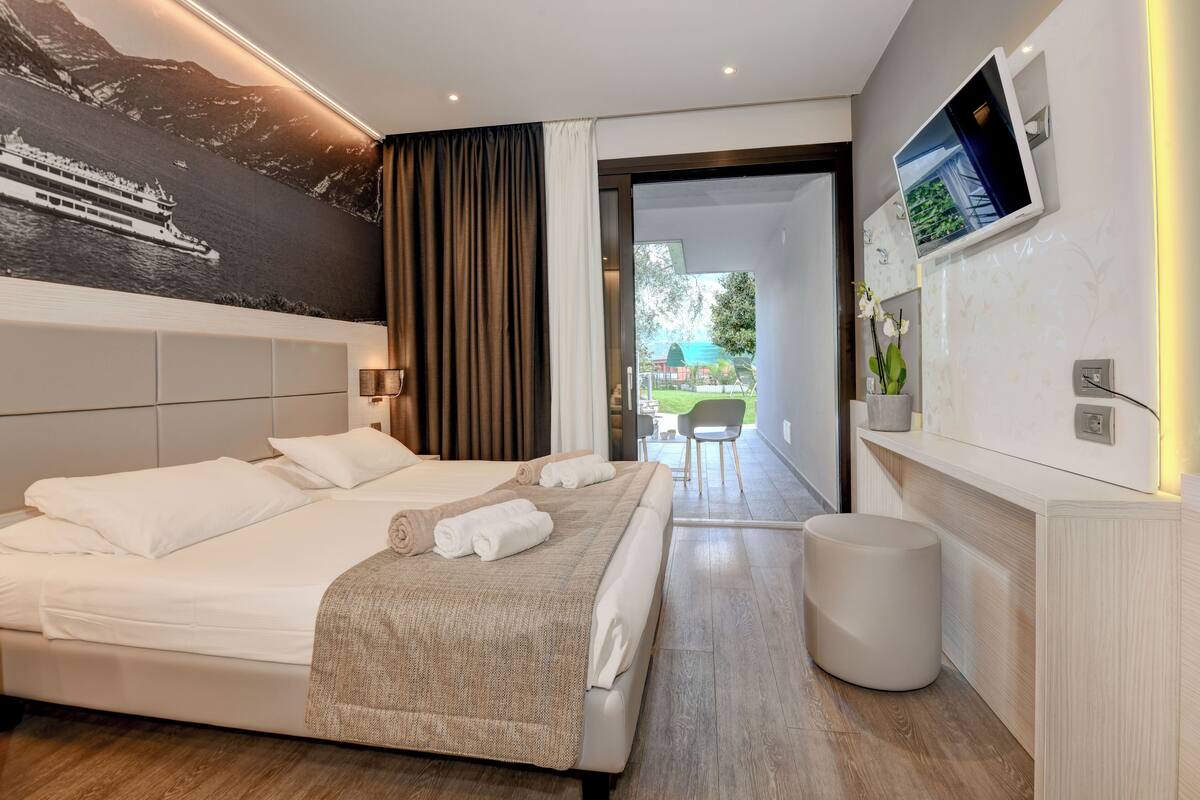 Una habitación de hotel moderna con una cama grande, un televisor de pantalla plana montado en la pared y vistas al exterior a través de una puerta abierta.