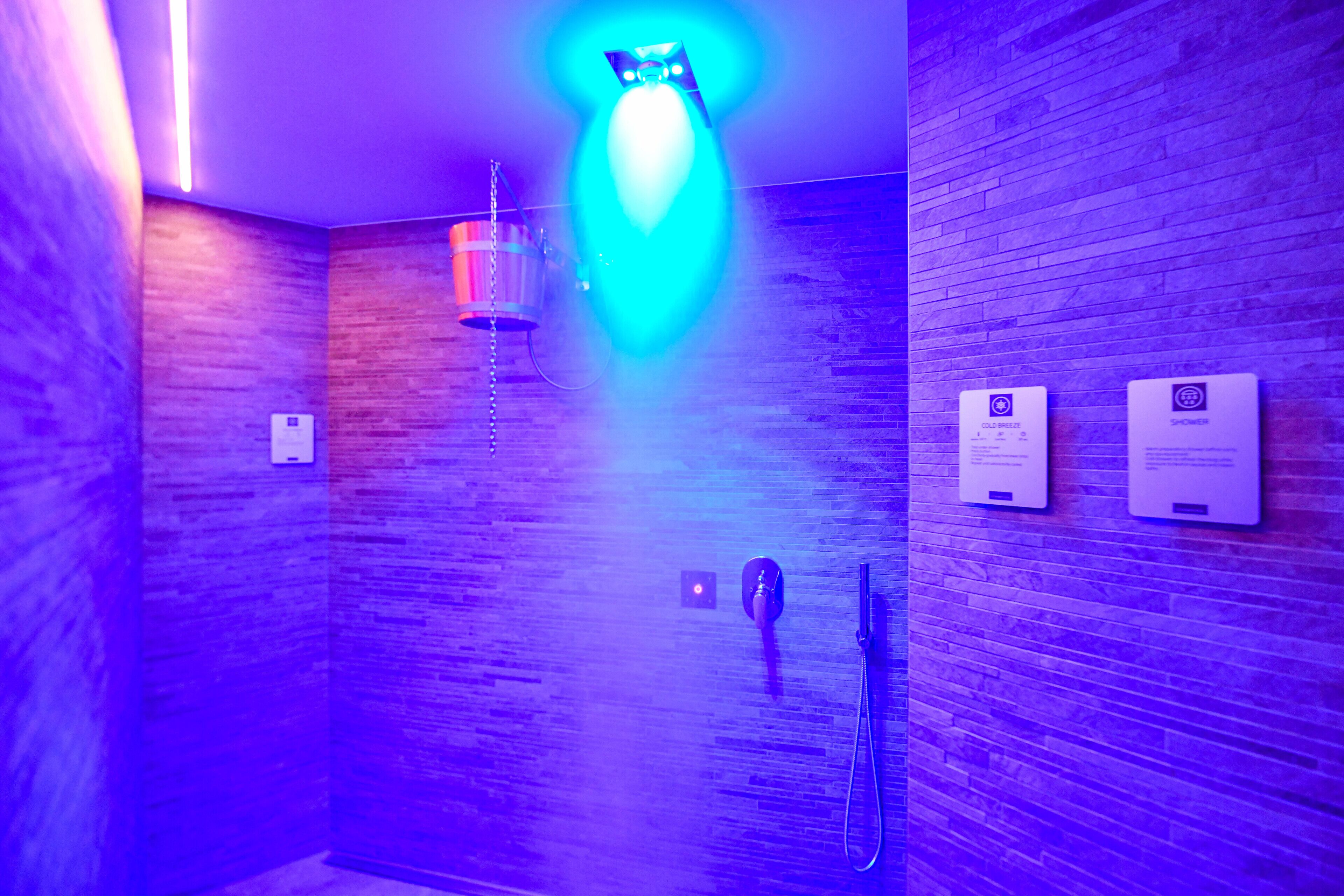 A bathroom with a wooden wall, a blue light fixture, and two informational signs.