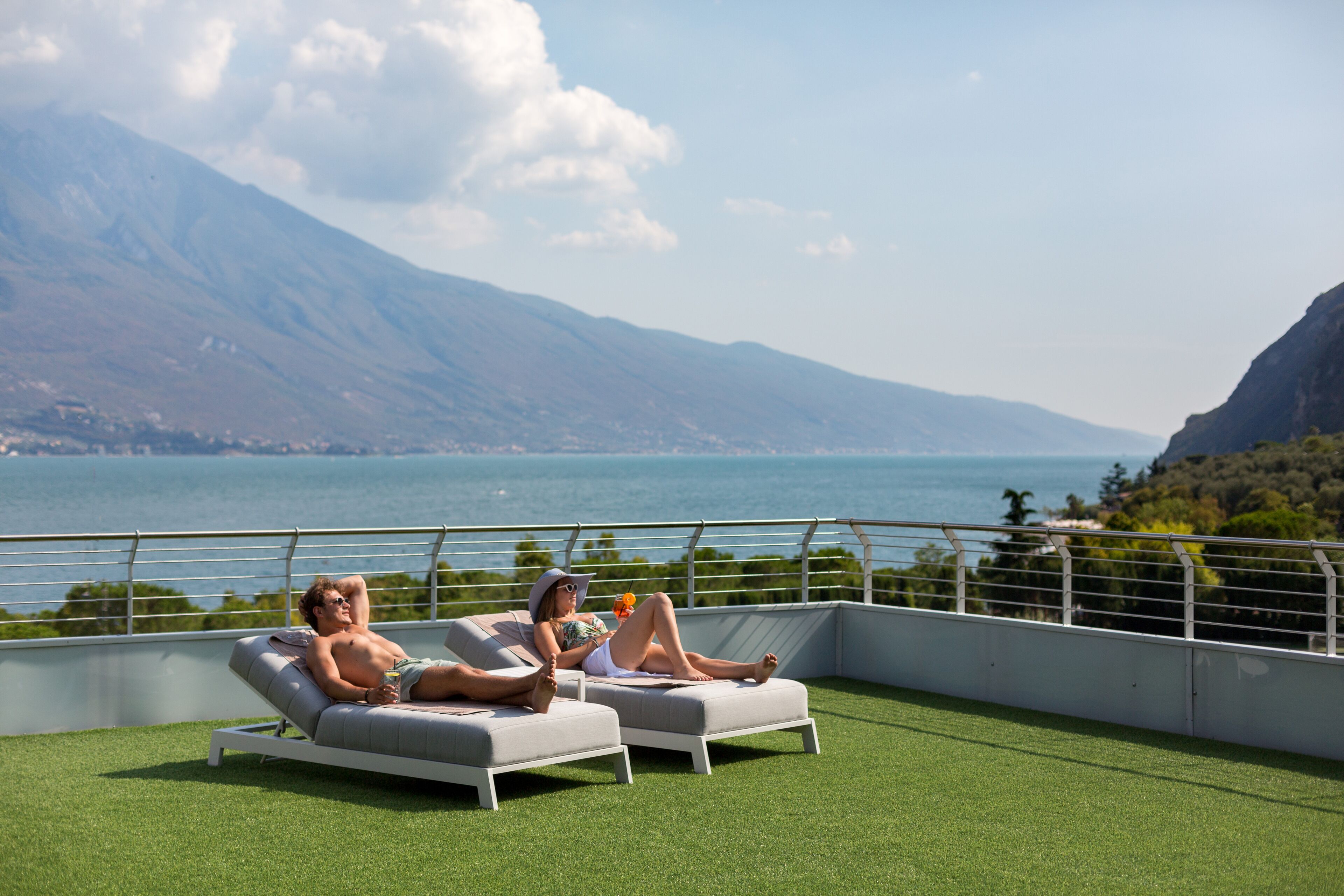 Two lounge chairs on a rooftop terrace with a view of the sea and mountains.