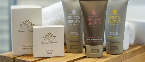 Un estante de madera con varios artículos de aseo personal, incluyendo una caja de Jabón Sabun Provencal Mansion, acondicionador Molton Brown Purifying y gel de baño y ducha Molton Brown.