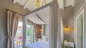 A four-poster bed with a canopy, a bedside table with a lamp, and a view of a balcony with flowers. - Provence Mansion Alacati (Cesme)