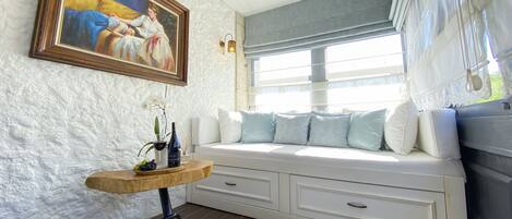 Una habitación acogedora con un sofá blanco, una mesita de madera con una botella y un vaso, y un cuadro en la pared.