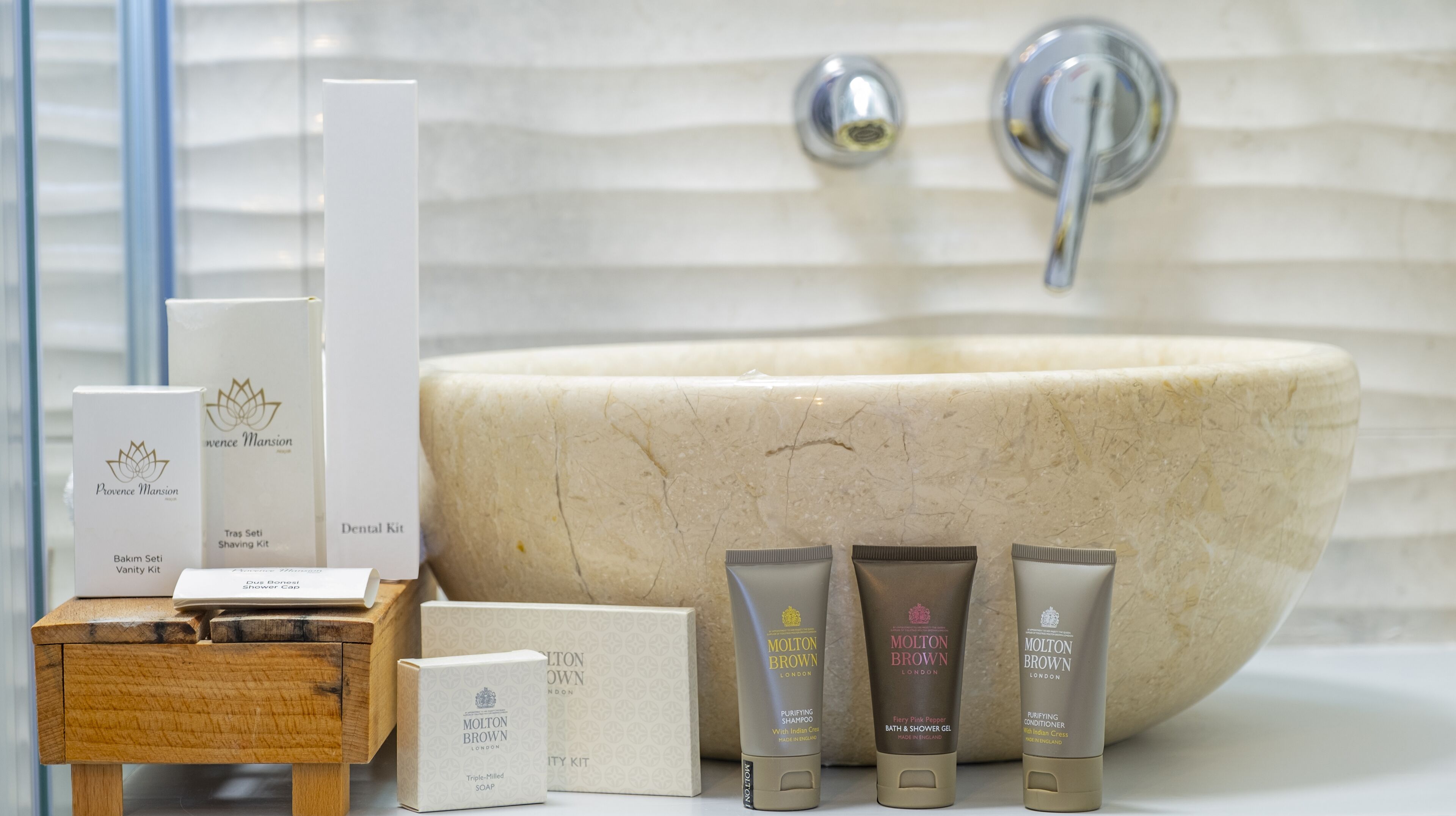 A bathroom with a large, oval-shaped sink, a wooden vanity, and toiletries including a shaving kit, soap, and shampoo.