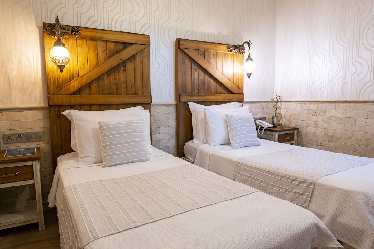 A hotel room with two beds, wooden headboards, and a nightstand with a lamp.