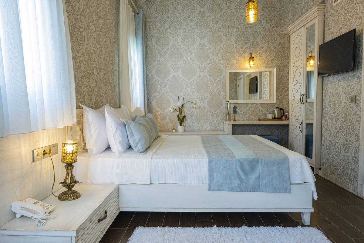 A bedroom with a bed, bedside table, lamp, and a mirror.