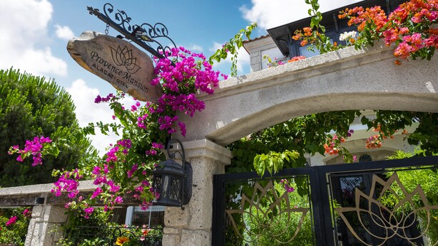 A stone archway with a sign for Provence Mansion Alacati Hotel, surrounded by vibrant bougainvillea flowers. - Provence Mansion Alacati (Cesme)