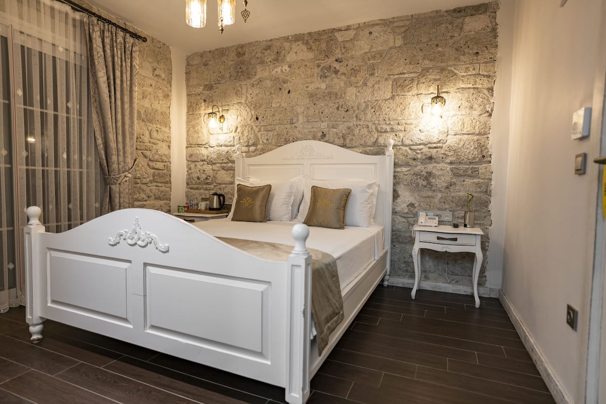 A bedroom with a stone wall, a white bed, and a bedside table.