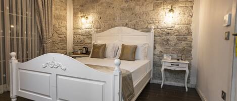 Quarto com parede de pedra, cama branca e mesa de cabeceira.