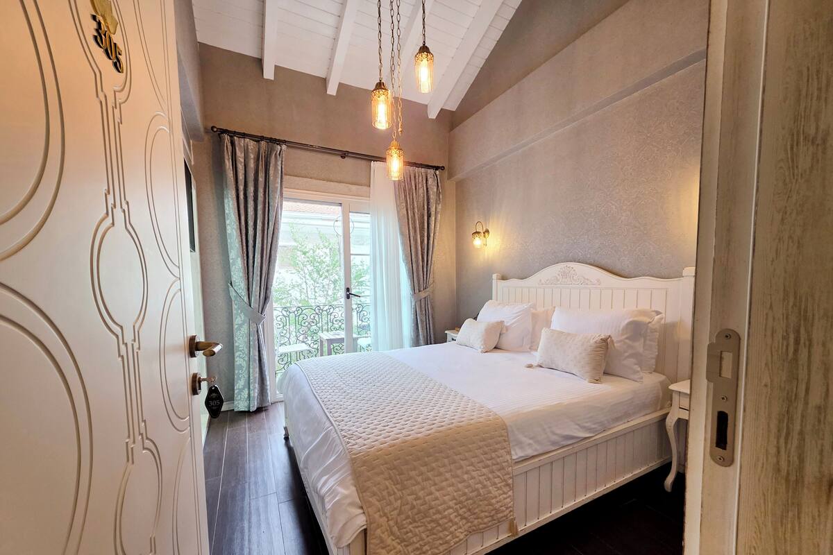 A bedroom with a bed, curtains, a nightstand, and a wall-mounted light fixture.