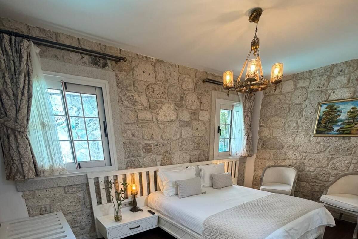 A bedroom with a stone wall, a bed with a white headboard, a nightstand, a chair, and a white rug.
