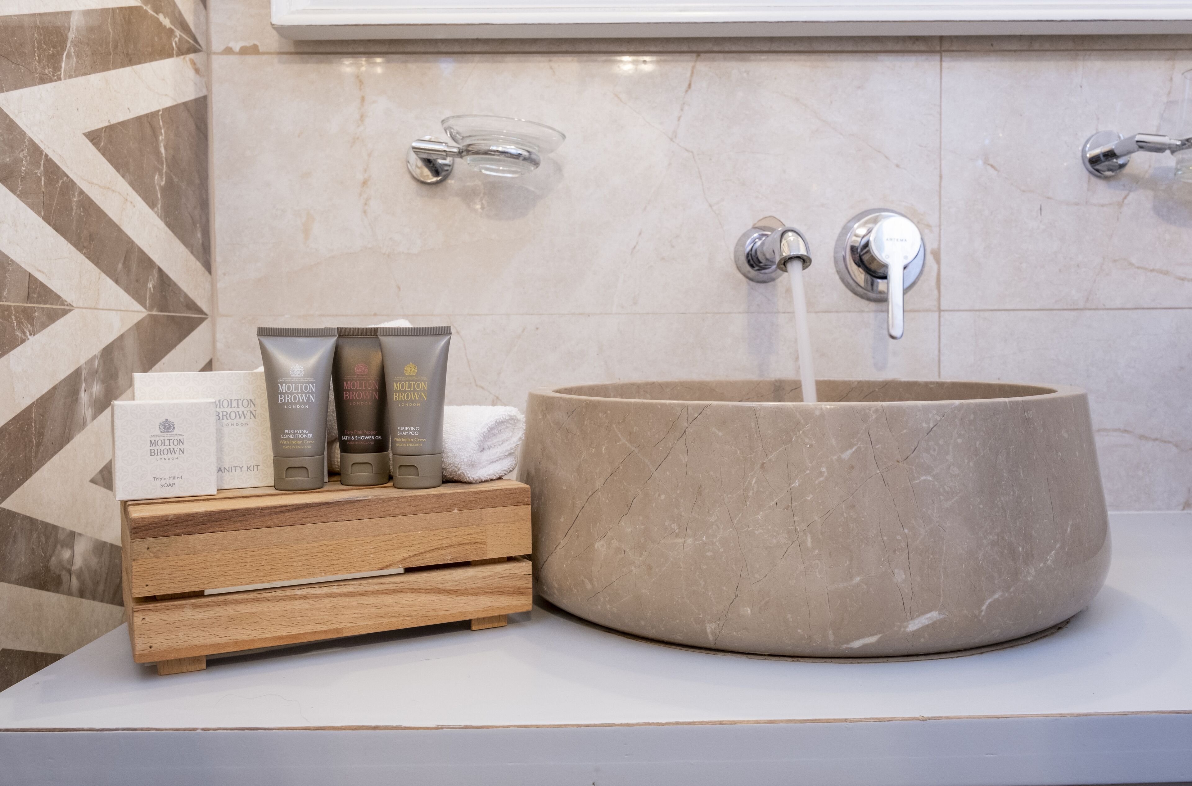 A bathroom with a large stone sink, two faucets, and a wooden vanity with toiletries.