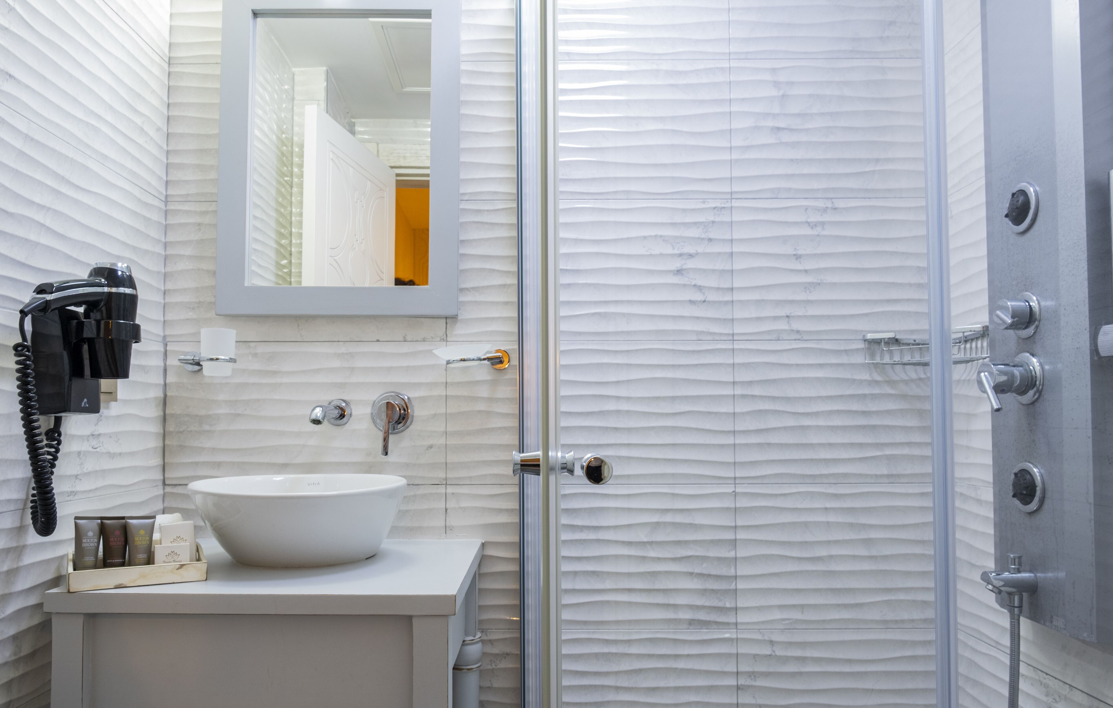 Un baño con lavamanos blanco, un espejo, un teléfono y zona de ducha.