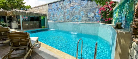 A swimming pool with lounge chairs, a bar area, and a mural wall.