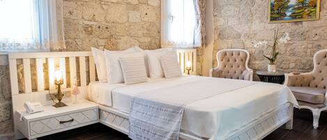 Une chambre avec un mur en pierre, un lit avec une literie blanche, une table de chevet avec un téléphone et une chaise.
