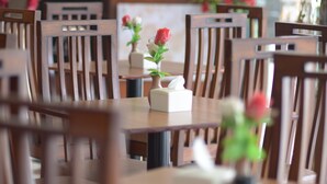 A dining area with wooden tables and chairs, some with vases of flowers. - Hyper Inn (Bandung)