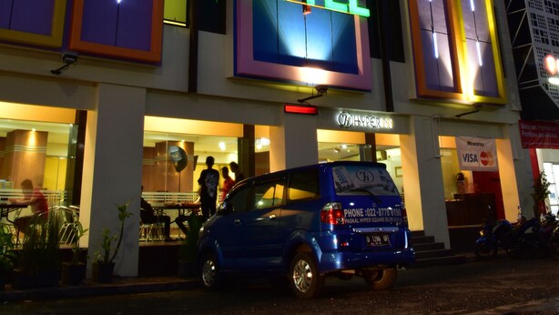 A hotel with a prominent 'HOTEL' sign, a visible pharmacy, and a blue van parked in front. - Hyper Inn (Bandung)