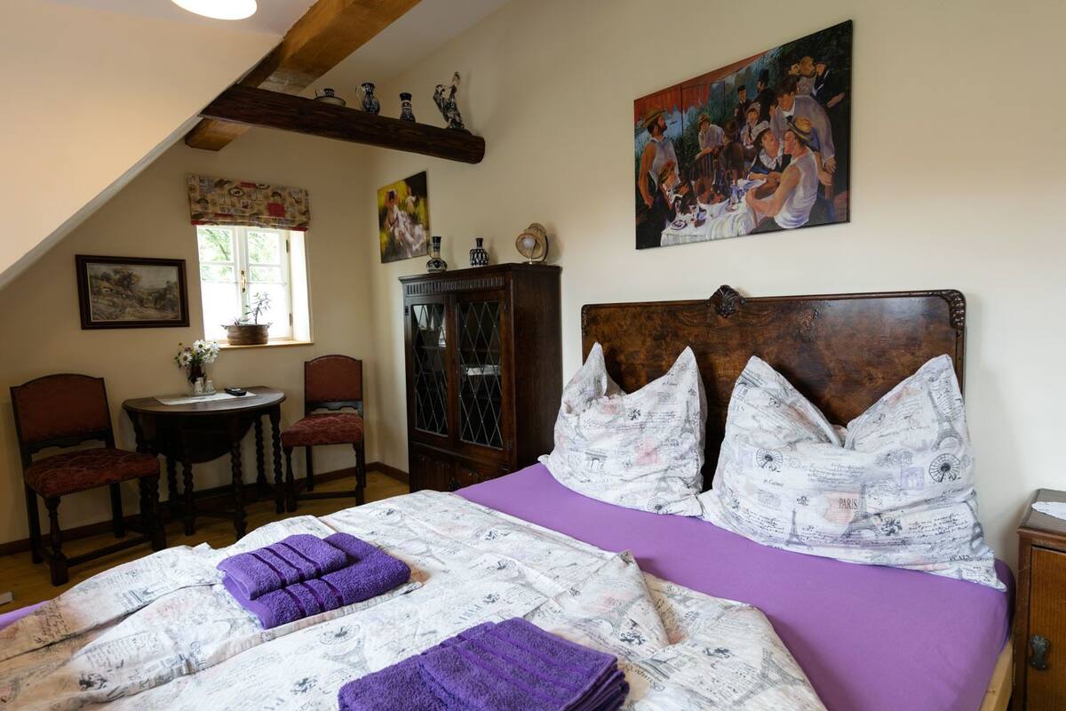 Um quarto com uma cama grande, cabeceira de madeira, janela com vista, uma cadeira, um armário e um quadro na parede.