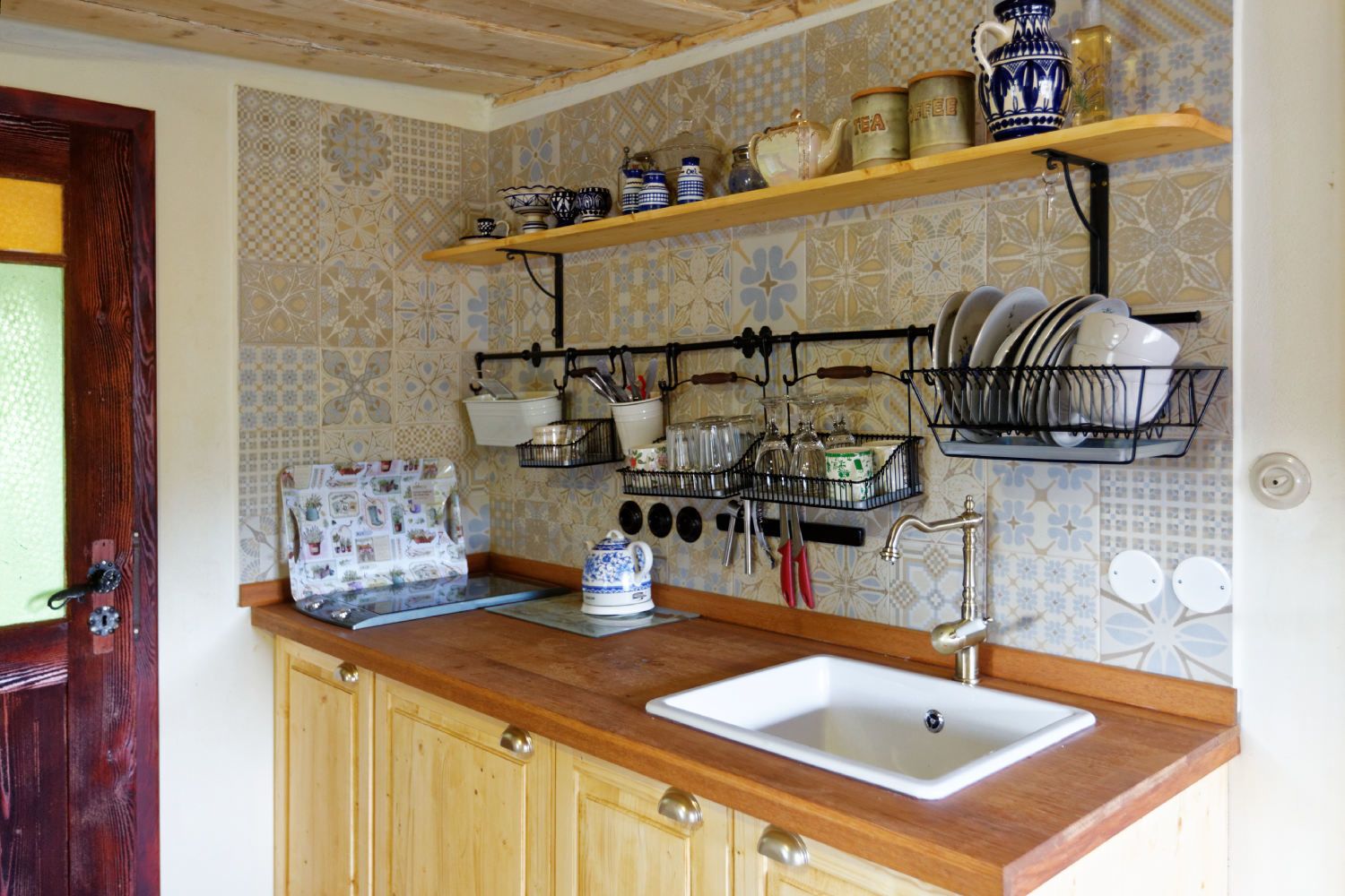 A kitchen with wooden cabinets, a sink, and various kitchen utensils and dishes on shelves.