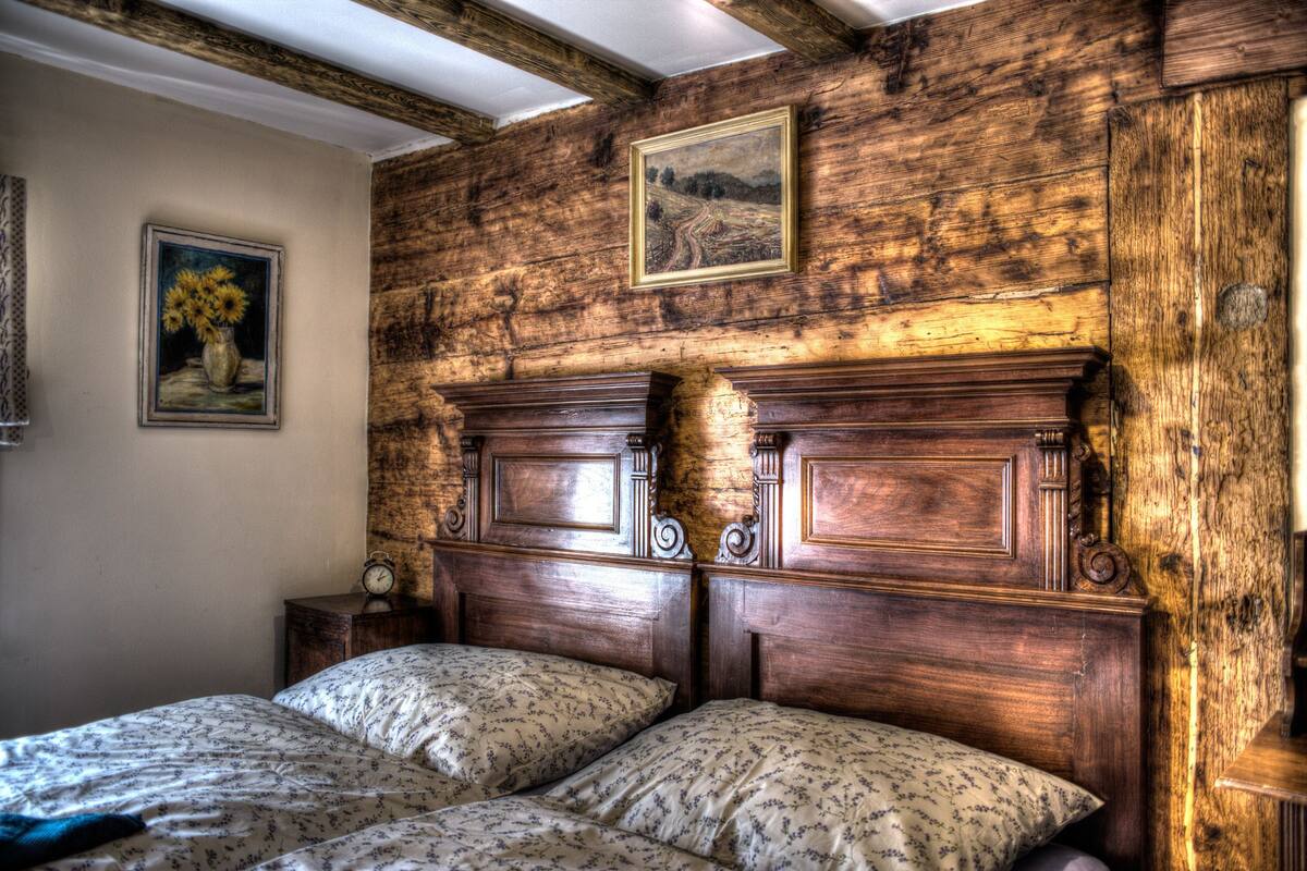 Quarto rústico com cabeceira de madeira, duas camas, mesa de cabeceira e um quadro na parede.