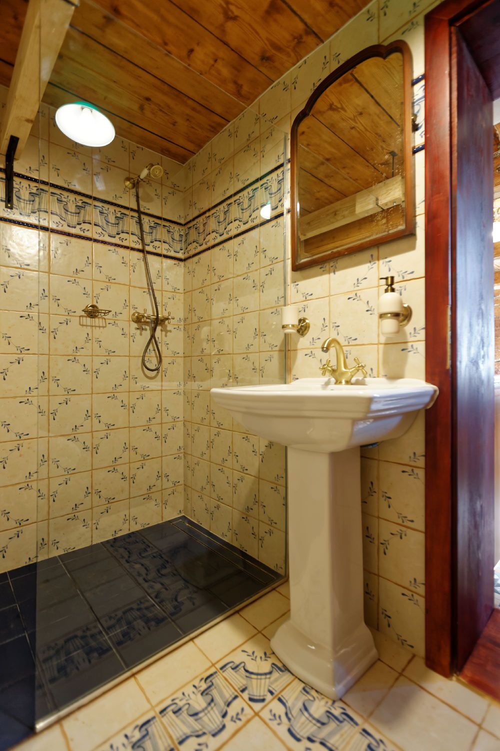 Ein Badezimmer mit gefliestem Boden, einem Waschbecken, einer Dusche und einem Spiegel.