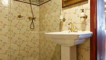 Ein Badezimmer mit gefliestem Boden, einem Waschbecken, einer Dusche und einem Spiegel.