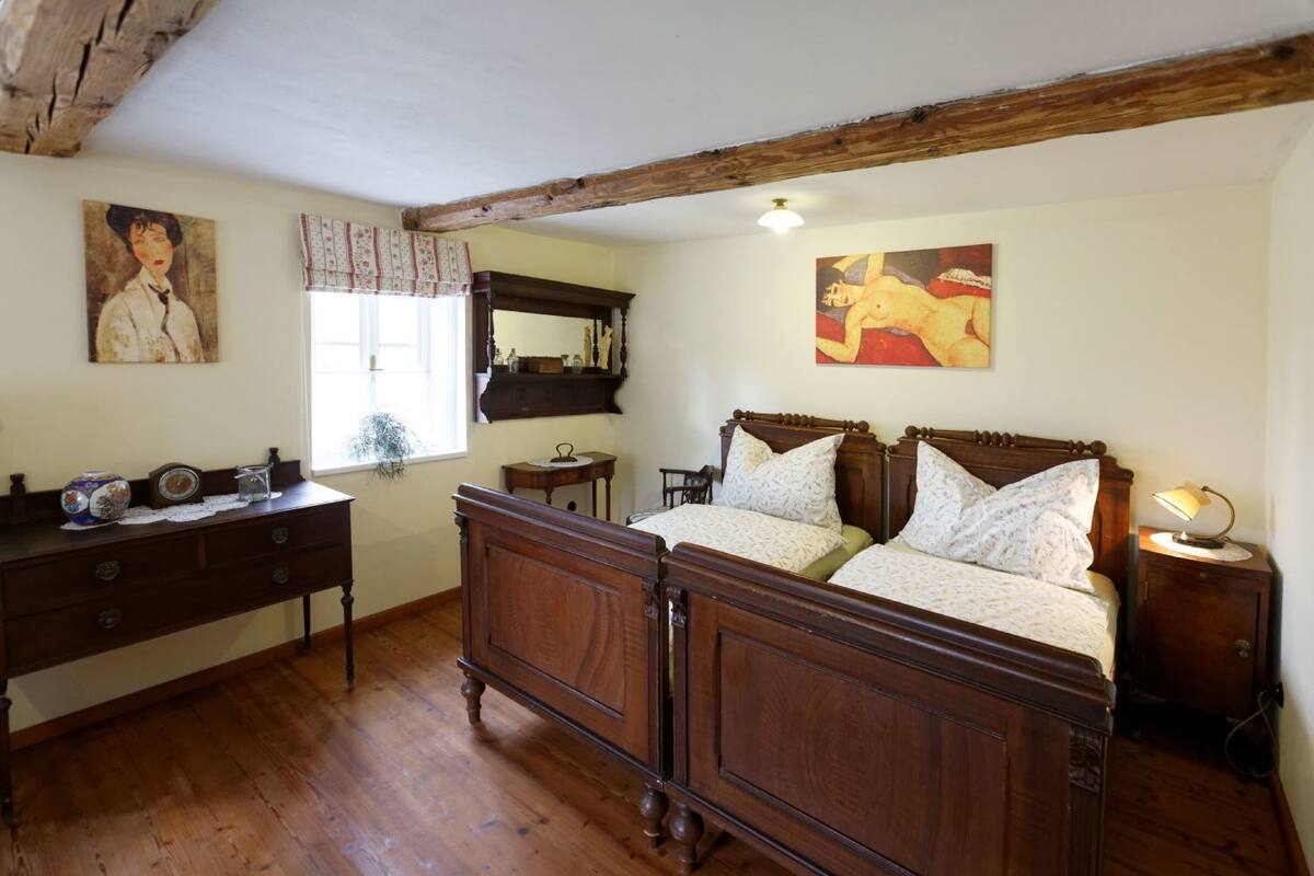 Quarto tradicional com cama de madeira, cômoda, espelho e obras de arte nas paredes.