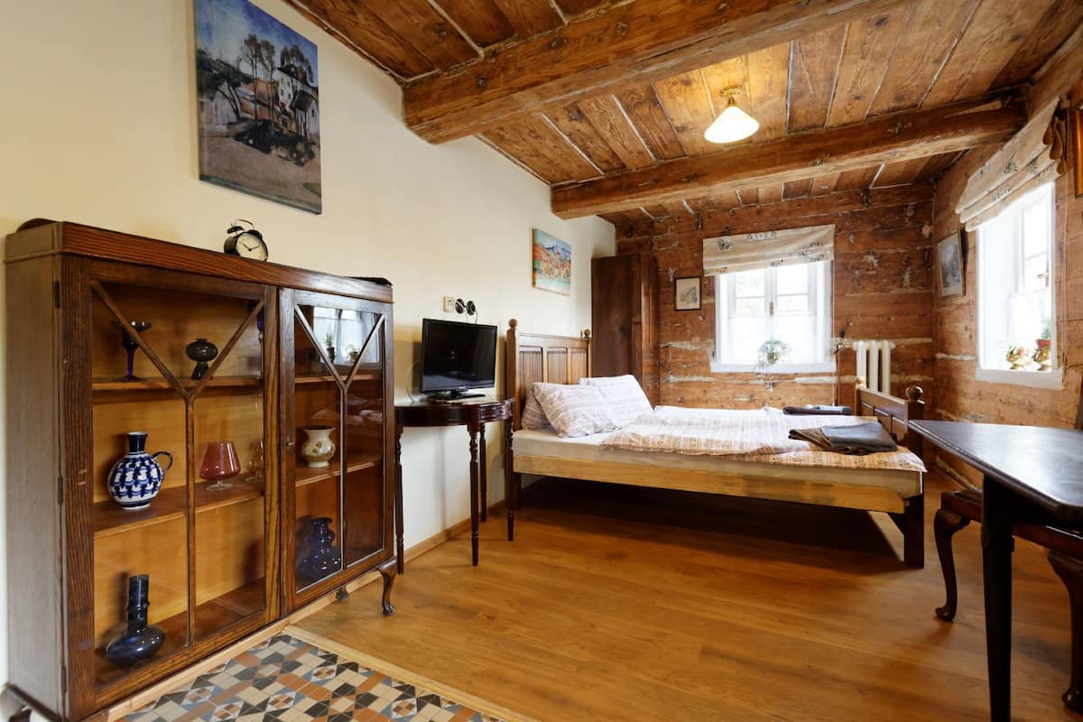 Quarto rústico com cama de madeira, televisão, aparador com portas de vidro e um quadro na parede.