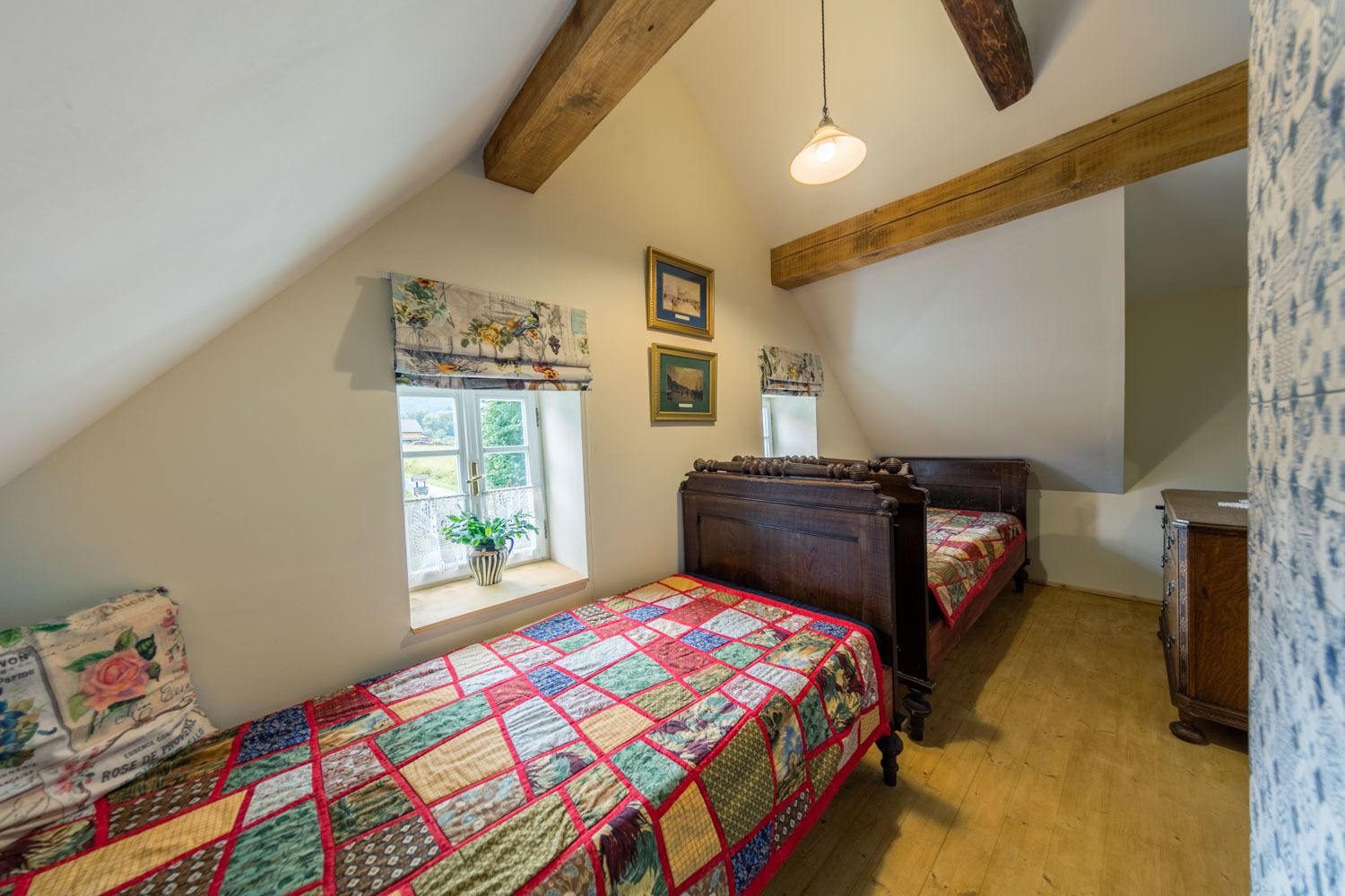 A bedroom with two wooden beds, a window with a view, and a ceiling with exposed beams.