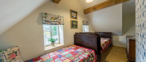 A bedroom with two wooden beds, a window with a view, and a ceiling with exposed beams.