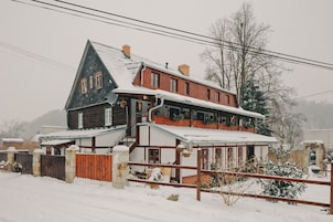Uma casa de dois andares com telhado inclinado, fachada de madeira e paisagem coberta de neve.