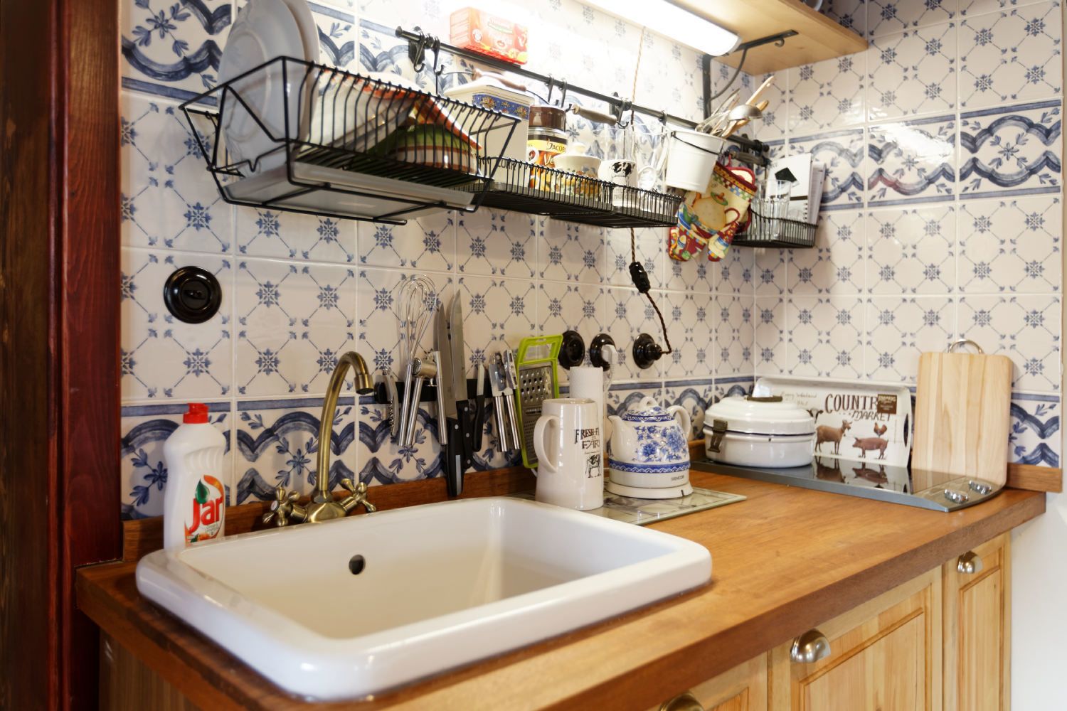 A kitchen with a white sink, a dish rack, and various kitchen utensils.