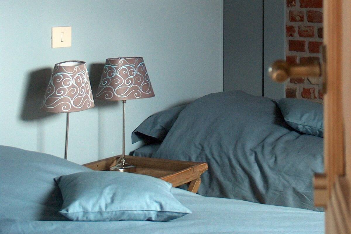 Quarto com cama, duas luminárias, mesa de cabeceira de madeira e parede de tijolos.