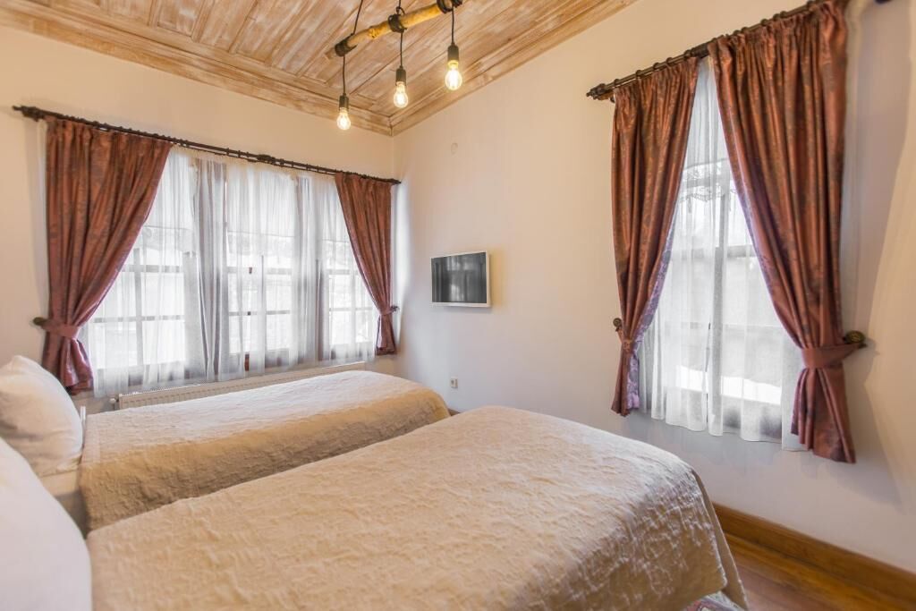 A room with two beds, wooden ceiling, and large windows with curtains.